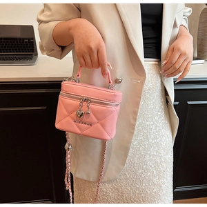 Close-up of pink quilted box bag with heart pendant and leather-woven chain strap