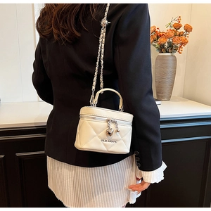 Detail of cream quilted box bag featuring heart pendant and silver chain strap