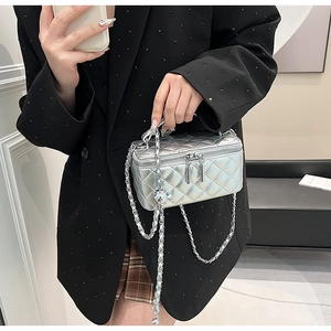 Silver quilted vanity bag with metal chain strap held by a model in a black suit