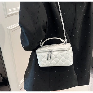 Detail of white quilted crossbody bag with silver zipper and woven chain strap
