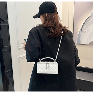 Detail view of white quilted crossbody bag with metal chain strap on model outfit