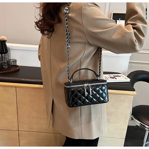 Detail of black quilted patent leather handbag with chain strap and silver hardware