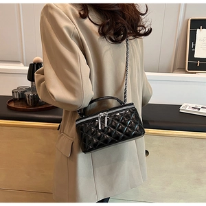 Detail of black quilted leather vanity bag with silver chain strap on model's shoulder