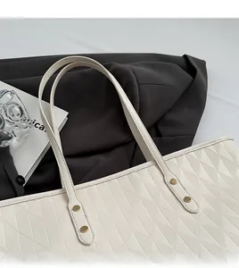 Detail of off-white tote bag featuring quilted diamond pattern and golden rivet accents