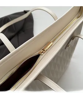 Close-up of smooth gold metal zipper and quilted texture on cream tote bag