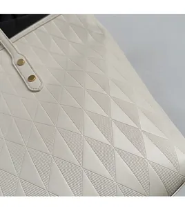 Detail of off-white tote bag showing geometric triangle embossing and gold rivets