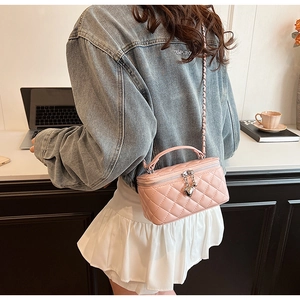 Detailed view of pink quilted handbag with metal handle and heart pendant in a cozy setting