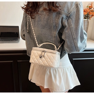 Detail of white quilted mini bag with silver heart charm and metal chain strap on leather