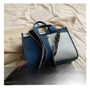Détails d'un sac cabas en denim bicolore avec fermoir rotatif doré sur lit blanc