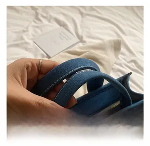 Gros plan des poignées du sac cabas en denim avec surpiqûres blanches et fermeture éclair