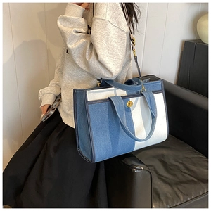 Détail d'un sac cabas en denim avec fermoir doré posé sur un canapé en cuir noir
