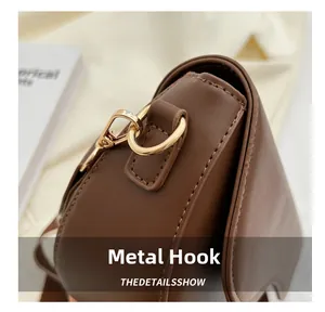 Detail of light gold hardware hook and D-ring on a brown leather crossbody handbag