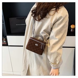 Close-up of brown quilted box bag with silver chain strap worn by a model in a room