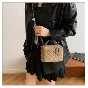 Detail of khaki quilted suede box bag with metal handle and chain strap on a model