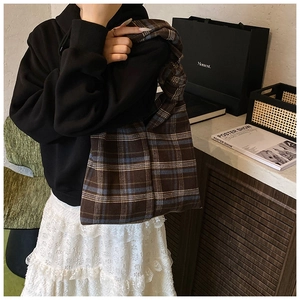 Brown and blue checkered knit tote bag shown worn by a model in a cozy indoor setting