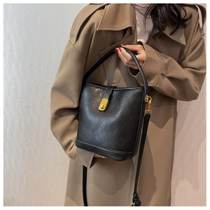 Detailed view of a black leather bucket bag with gold lock worn with a khaki trench coat