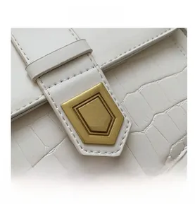 Close-up of white crocodile pattern leather saddle bag with gold pentagon lock buckle