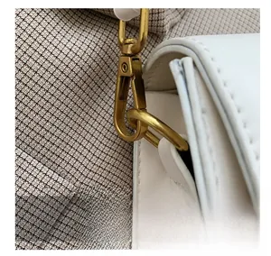 Close-up of golden metal hooks and D-ring on white leather saddle bag shoulder strap