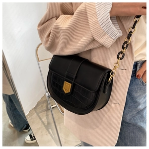 Detail of black saddle bag featuring gold metal buckle and chunky chain strap on model