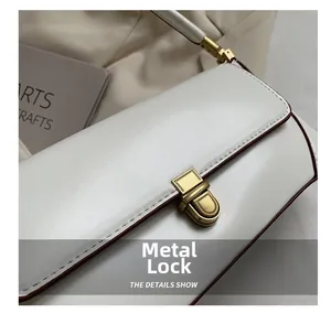 Close-up of golden hardware clasp and brown edge finish on white faux leather tote bag