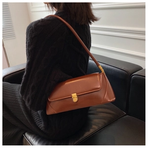 Brown rectangular shoulder bag with golden metal buckle clasp on minimalist black sofa