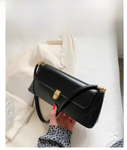 Detail of minimalist black baguette shoulder bag with elegant gold metal lock clasp