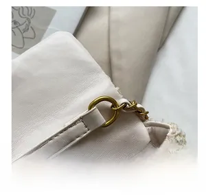Detail of gold metal ring on white leather and light tweed crossbody bag texture