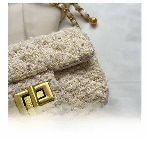 Macro view of creamy tweed fabric and elegant gold turn-lock buckle on the handbag