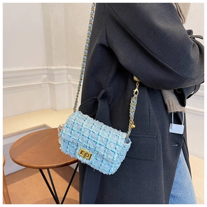 Detail shot of light blue tweed crossbody bag with golden chain and metal lock on a model