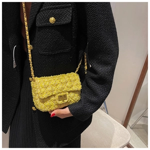 Detail of yellow tweed crossbody bag with gold square buckle and chain strap on black coat
