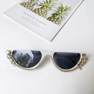 Detail von weißer Cat-Eye-Sonnenbrille mit doppelten Kristallsteinen und dunklen Gläsern