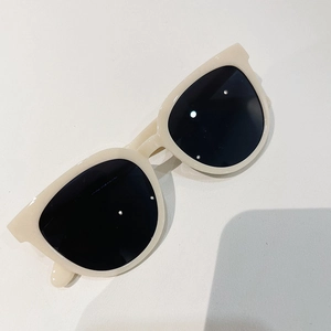 Detailed close-up of retro cream oval sunglasses with dark lenses on white background