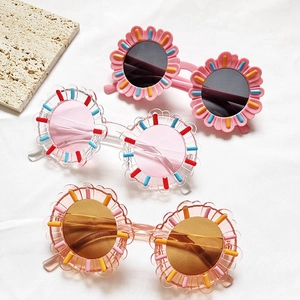Three pairs of flower-shaped kids sunglasses in candy colors on white fabric background