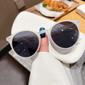 Lunettes de soleil rétro rondes beige mat avec verres foncés dans un café