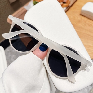 Gros plan de lunettes de soleil rondes mates avec verres foncés sur un étui texturé blanc