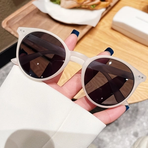 Détail de lunettes de soleil rondes crème avec rivets métalliques et verres UV