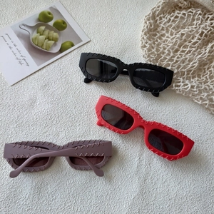 Detail of square sunglasses with wavy embossed frames in black, red, and purple colors