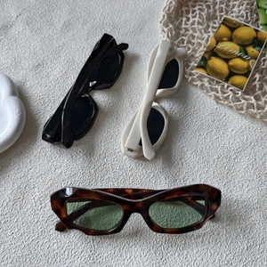 Trois lunettes de soleil rétro en noir, crème et écaille sur un fond de tissu minimaliste