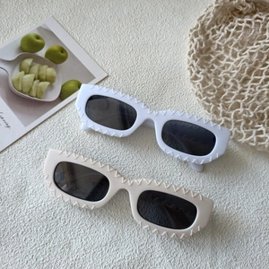 Close-up of wavy-edge sunglasses in white and cream beige colors with a summer aesthetic