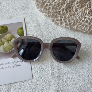 Detail view of retro oversized grey acetate sunglasses with round lenses on a white textured background