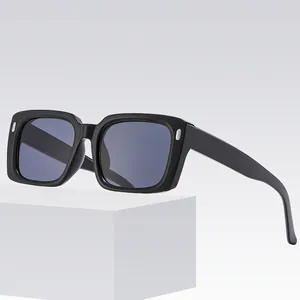 Lunettes de soleil carrées noires avec rivets argentés sur socle blanc, style rétro chic