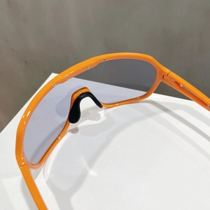 Close-up of bright orange sports sunglasses frame with black nose pads and screw details