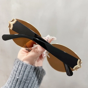 Close-up of amber oval rimless sunglasses featuring luxury gold C-shaped metal decor