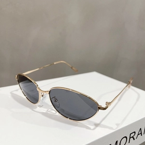 Detail view of gold metal cat-eye sunglasses with dark lenses on a minimalist white stand