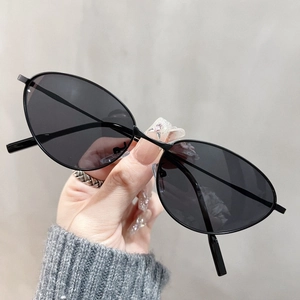 Close-up of slim metal cat-eye sunglasses with dark lenses held by hand against a grey wall