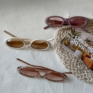 Trois lunettes de soleil ovales rétro en rose, crème et marron sur fond blanc épuré