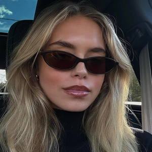 Retro oval cat-eye sunglasses with narrow black frames worn by a model in a car setting