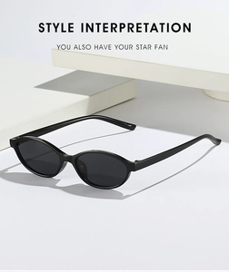 Detail view of oval black frame sunglasses with dark lenses on a minimalist white stand