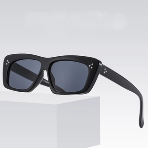 Lunettes de soleil carrées noires avec trois points métalliques sur socle géométrique