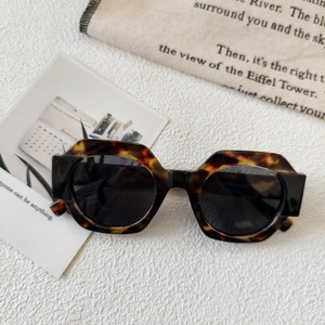 Detail of tortoiseshell hexagonal frame sunglasses on a minimalist white texture background